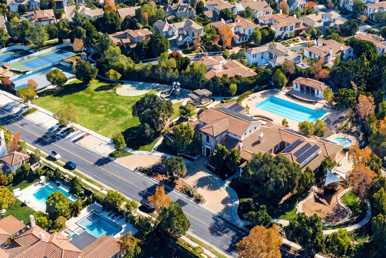 Aerial view of a Calabasas community with a shared pool, tennis courts, and homes with private backyard pools