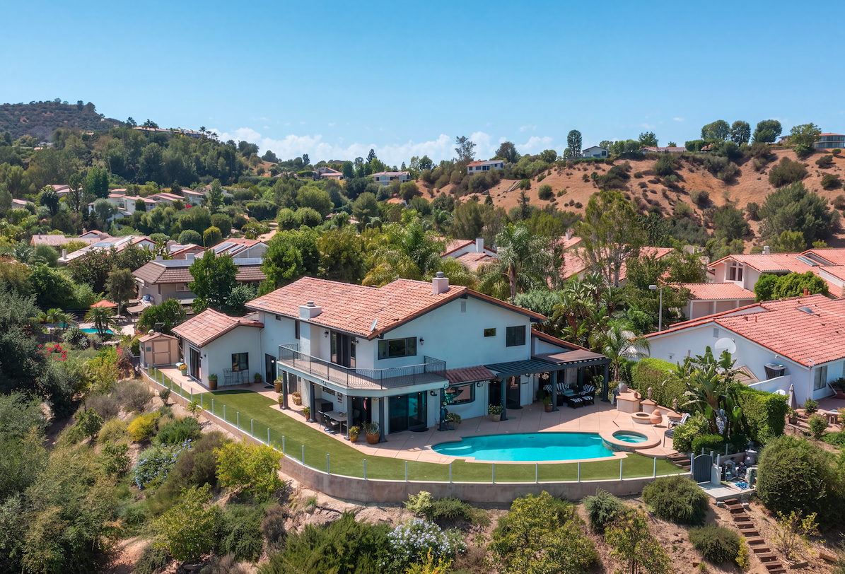 Aerial view of a Calabasas hillside home with a pool and patio backing to open brush