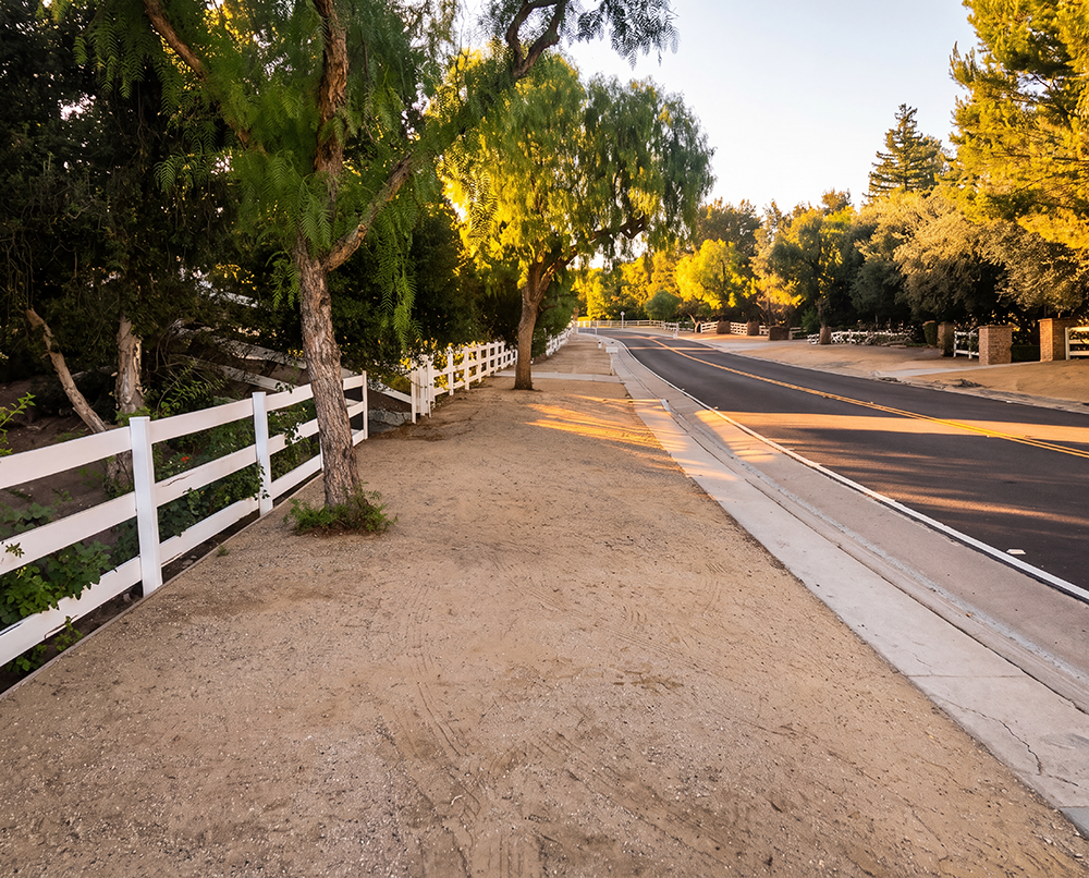 Dirt bridle trail and white ranch fence along a tree-lined Hidden Hills street