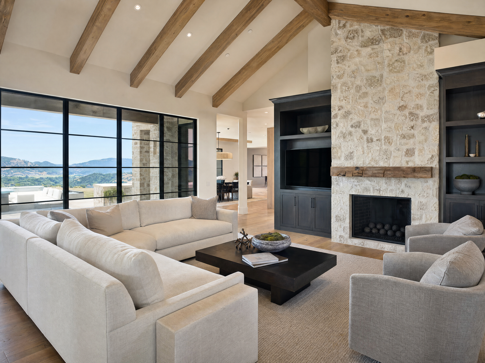 Luxury living room with beamed ceiling, stone fireplace, and canyon views